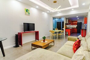 A modern living room with a flat-screen TV, a coffee table, and a sofa. There is a dining area with a table and chairs, and a kitchen in the background. - Relaxing Condo Stay in Seibu Tower (Taguig City)