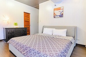 A bedroom with a bed, a dresser, a door, and a wall-mounted painting. - Relaxing Condo Stay in Seibu Tower (Taguig City)