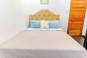 A bed with a tufted headboard, two pillows, and a neutral-colored bedspread in a room with white walls and a wooden door. - Relaxing Condo Stay in Seibu Tower (Taguig City)