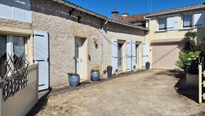 A narrow alleyway with a rustic stone building, a wooden gate, and potted plants.