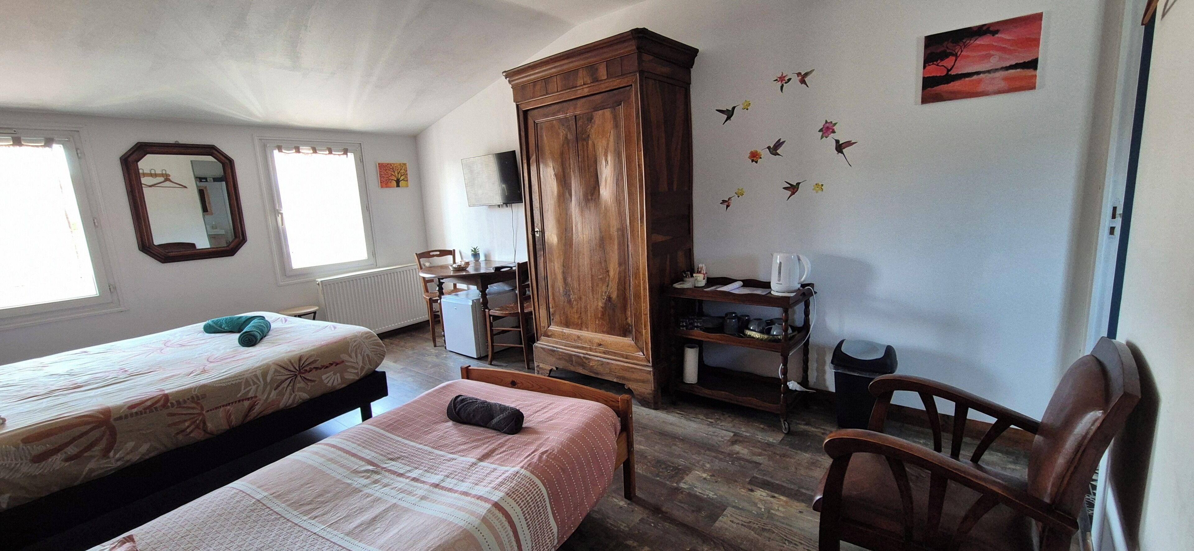 Ein Zimmer mit zwei Betten, einem Holzschrank, einem Schreibtisch mit Stuhl, einer Heizung und einer Wand mit Vogelmotiven.
