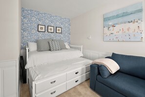 Ein Schlafzimmer mit einem Bett, einem Schminktisch, einem blauen Sofa, blumigem Wandpapier und einem Bild an der Wand.