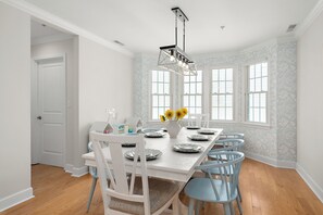 Ein Esszimmer mit weißem Tisch, gedeckt für sechs Personen, umgeben von sechs Stühlen, einer Chandelüster und einer Blumenvase.