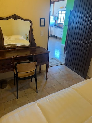 A hotel room with a wooden desk, a chair, a bed, and a view of the outside.