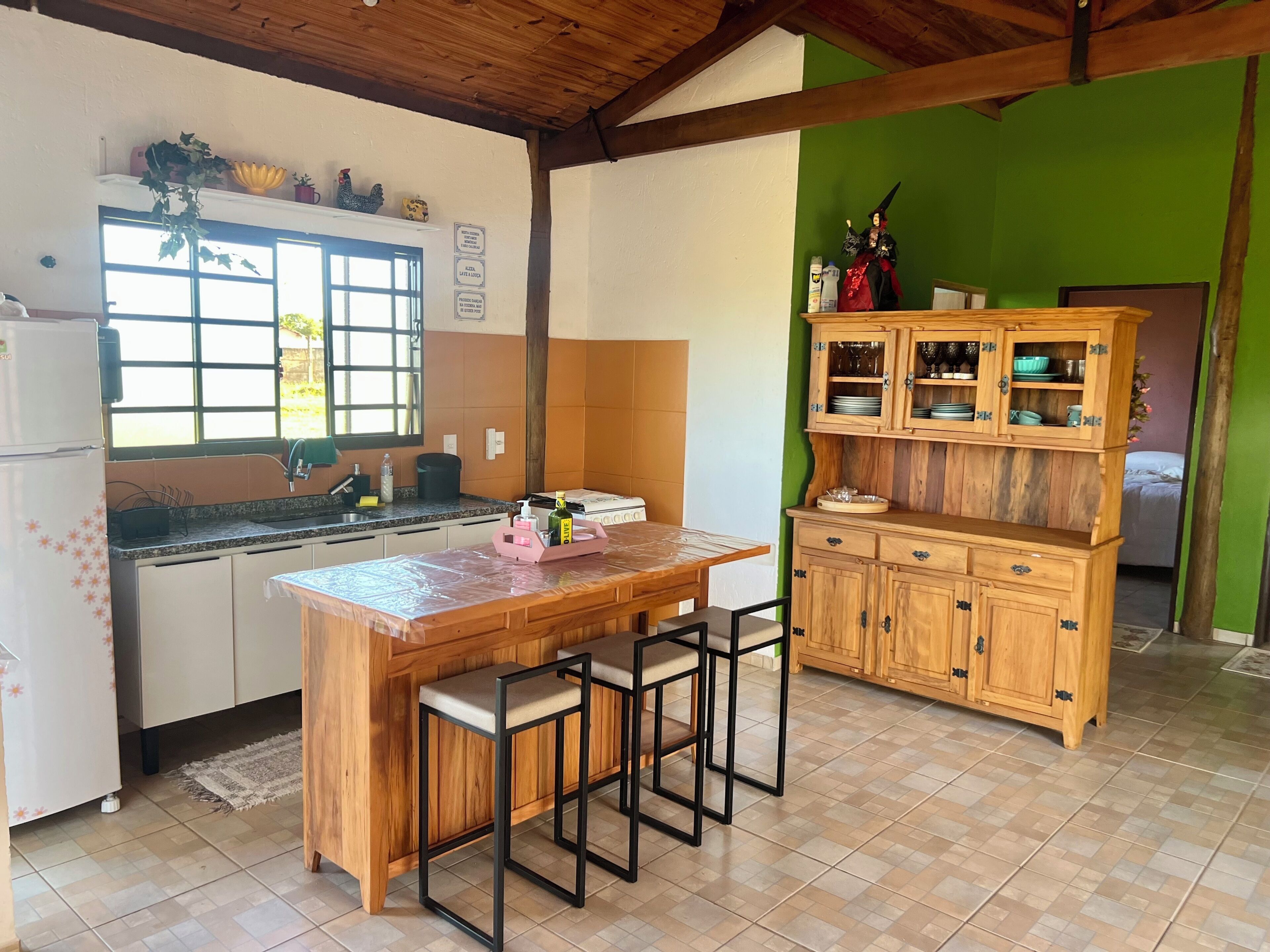 A kitchen with a wooden island, bar stools, a refrigerator, and a green accent wall.