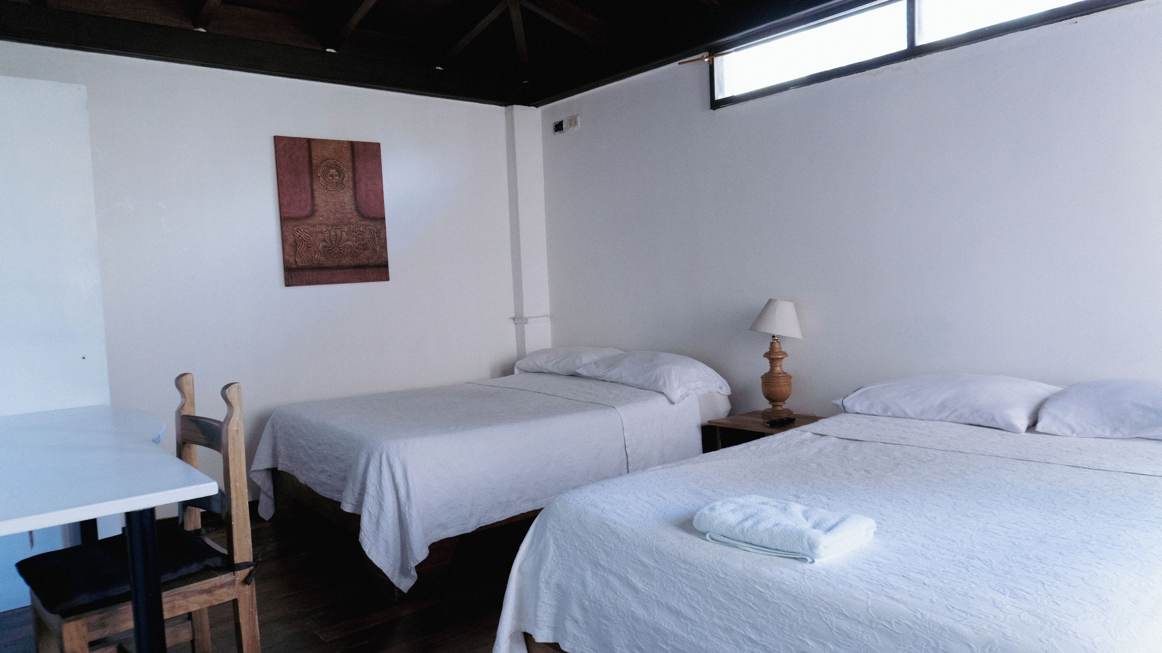 A room with two single beds, a table with a chair, and a wall-mounted lamp.