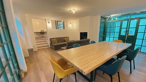 Una sala de estar moderna con una mesa de comedor de madera, sillas amarillas y azules, un sofá y una escalera que lleva a otro nivel.