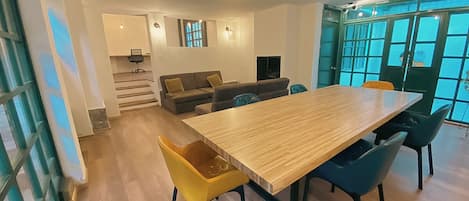 A modern living room with a wooden dining table, yellow and blue chairs, a sofa, and a staircase leading to another level.