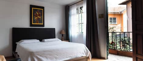 A bedroom with a bed, a bedside lamp, a window with curtains, and a view of the outside.