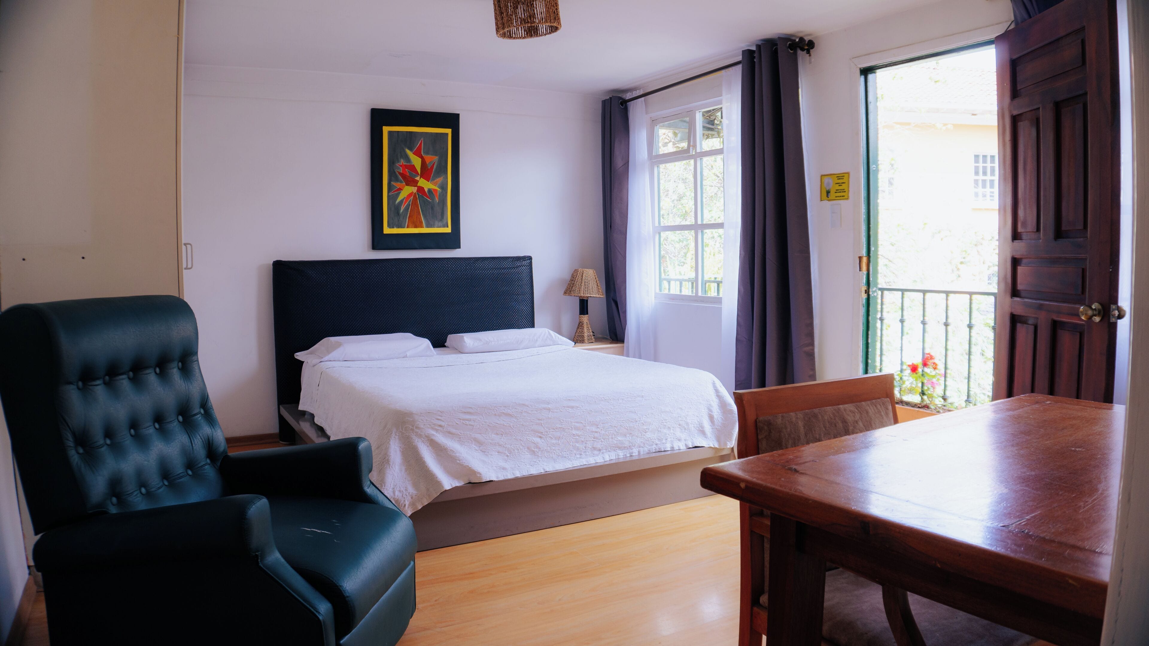A hotel room with a bed, a chair, a table, and a window with curtains.