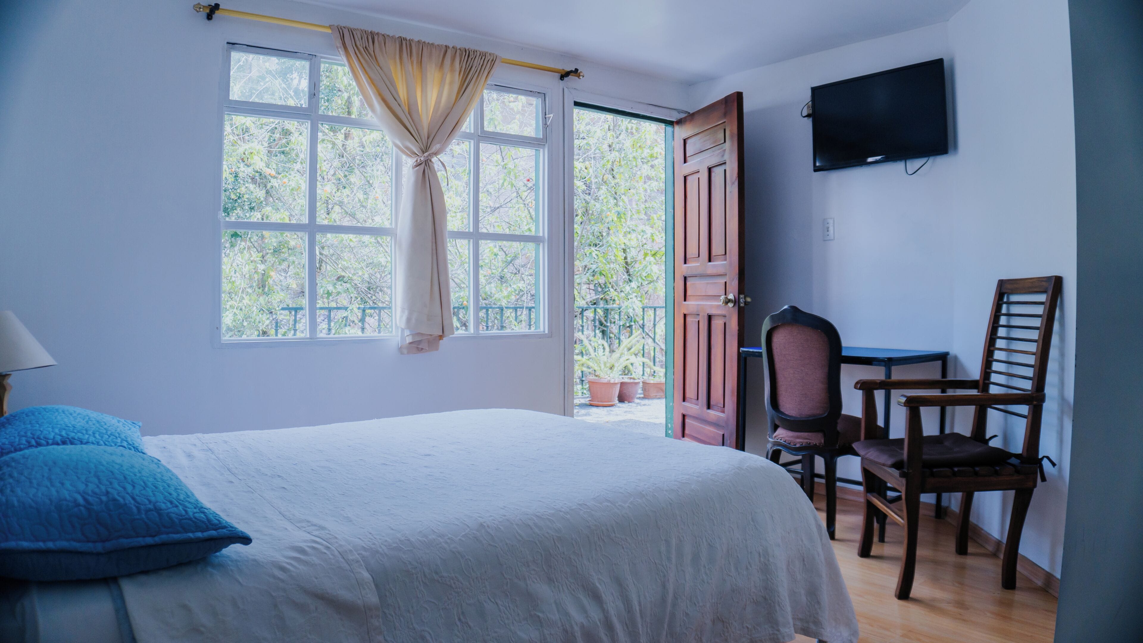 Un dormitorio con cama, escritorio, silla, televisor y ventana con cortinas.