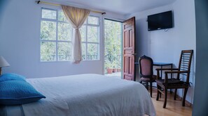 Un dormitorio con cama, escritorio, silla, televisor y ventana con cortinas.