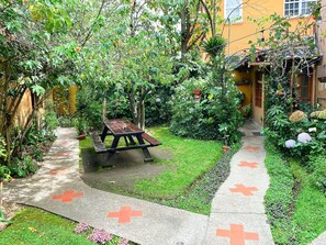 A garden with a picnic table, a pathway with red crosses, and a building in the background. - Colibrí Home Quito (Quito)
