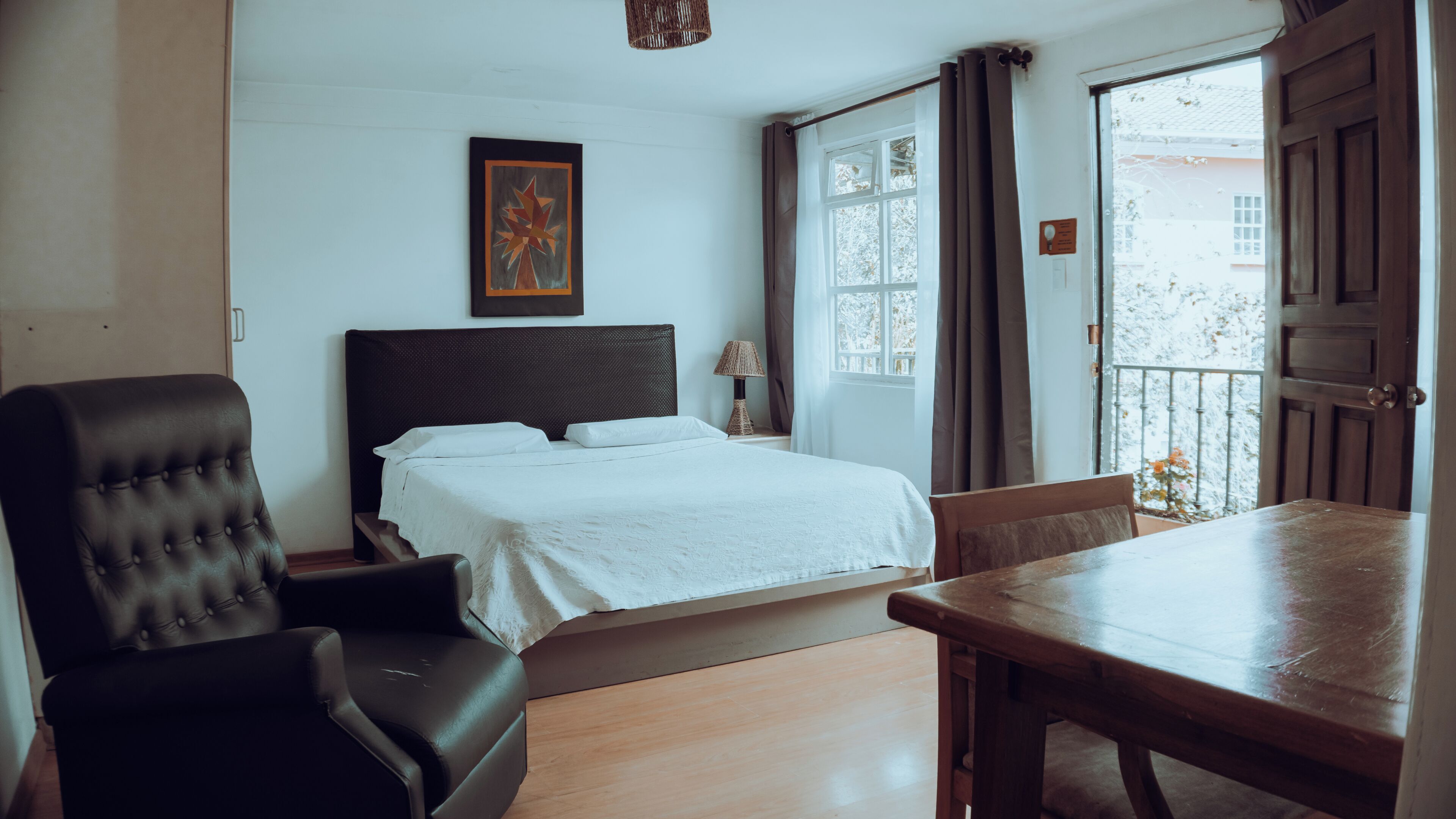 A bedroom with a bed, a chair, a table, and a window with curtains.
