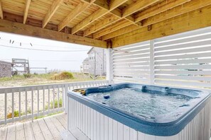 Eine Holzterrasse mit Whirlpool, weißen Geländern und Blick auf Strand und Häuser.