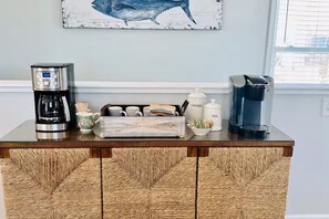 Una encimera de cocina con cafeteras, una jarra de café, tazas y un adorno.