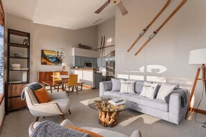 A modern living room with a grey sofa, a coffee table, and a dining area with a yellow chair. - Bluffs Penthouse - Luxe 3 Bedroom - Ski in Ski out (Whistler)