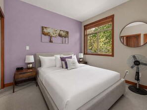 A bedroom with a large bed, two bedside tables with lamps, a wall-mounted mirror, and a window with a view of greenery. - Bluffs Penthouse - Luxe 3 Bedroom - Ski in Ski out (Whistler)