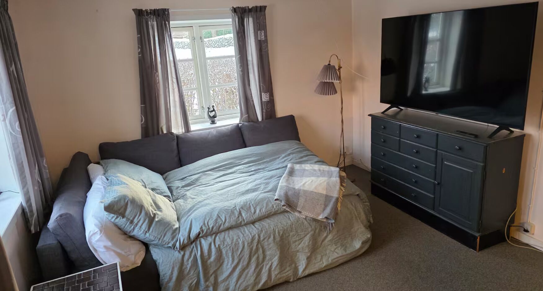Ein Schlafzimmer mit einem Bett, einem Schminktisch, einem Fernseher und einem Fenster mit Vorhängen.