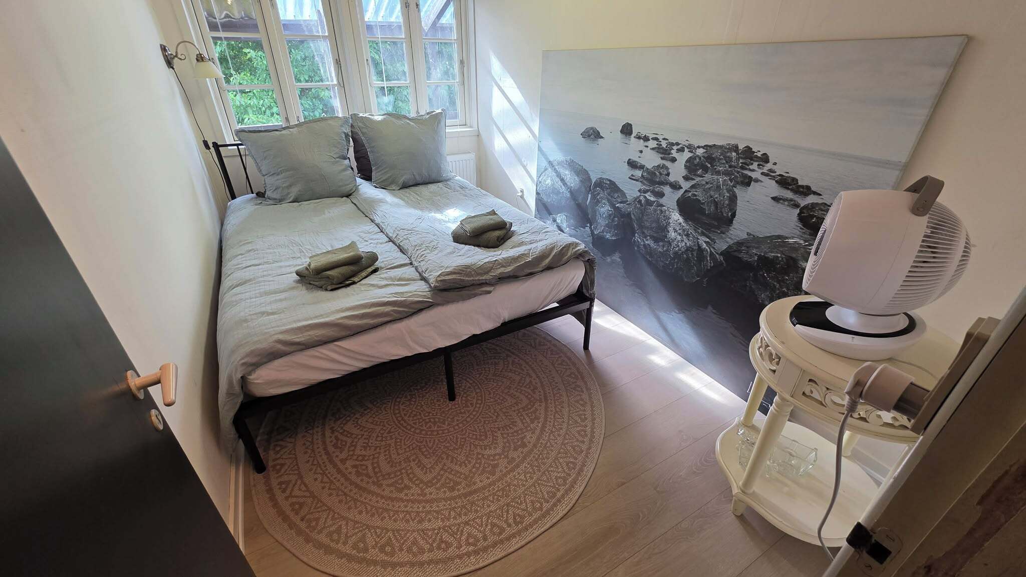 Et soveværelse med en seng, et tæppe, et maleri og en ventilator.