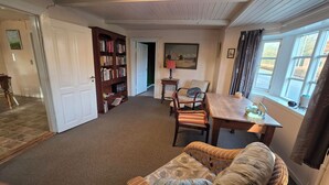 A cozy living room with a fireplace, a bookshelf, a dining table, and a comfortable sofa. - Historical Bullfinch Cottage - Amazing Day Trips! Minutes from Beach! (Tim Kirkeby)