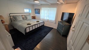 A bedroom with a bed, a dresser, a television, and a window with curtains.