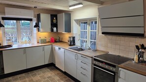 Una cocina con gabinetes blancos, horno empotrado, cafetera y ventana con vista a árboles.