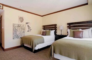 Une chambre d’hôtel avec deux lits, une table de chevet avec une lampe et des œuvres d’art accrochées aux murs.
