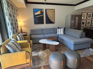 Un salon moderne avec un canapé d’angle, un fauteuil jaune, des poufs, une table basse et des œuvres d’art accrochées au mur.