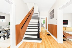 Eine Treppe mit Holzvertäfelung und schwarzen Geländern, die zu einer Küchenzeile mit weißen Schränken und einem Essbereich mit gedecktem Tisch für zwei Personen führt.