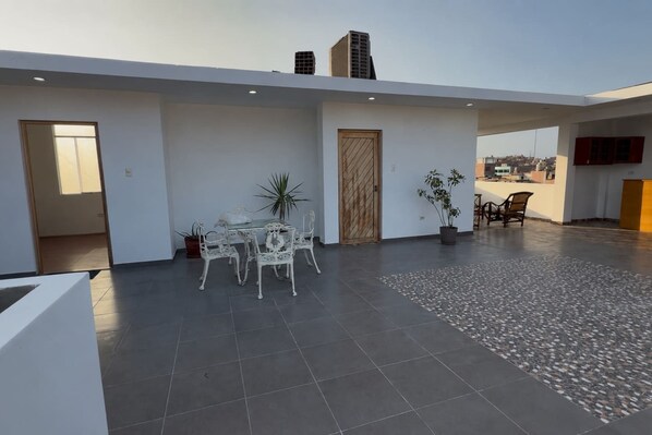 An open-plan living area with a dining set, potted plants, and a view of the cityscape.