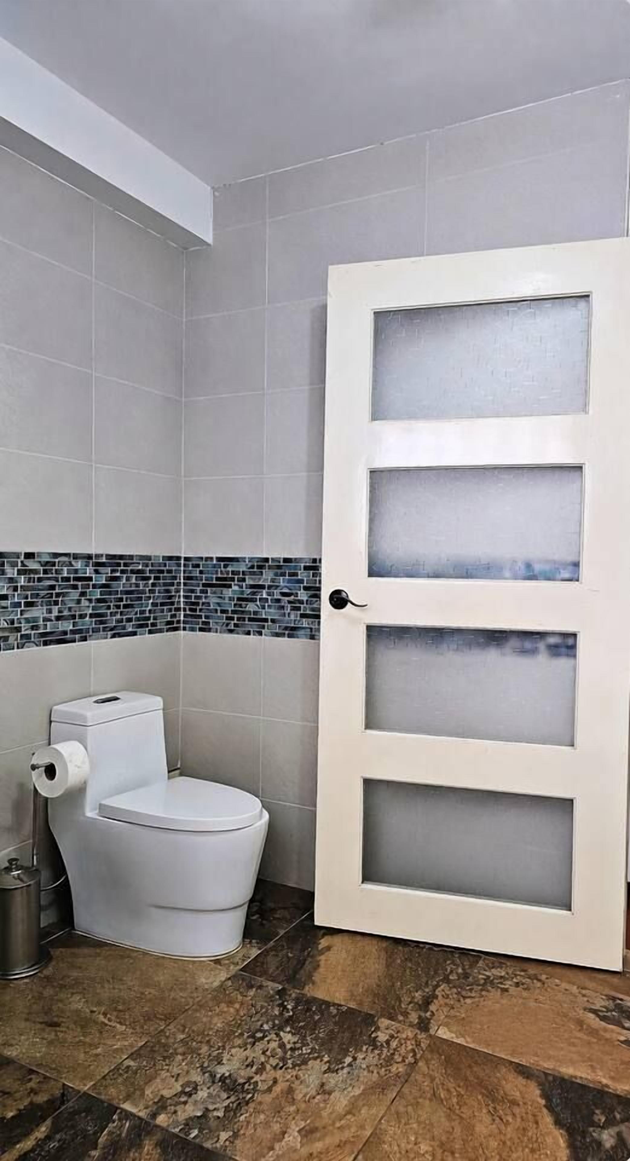 A bathroom with a toilet, a trash bin, and a door with frosted glass panels.