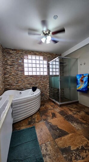 A bathroom with a stone wall, a glass shower enclosure, a white bathtub, and a ceiling fan.
