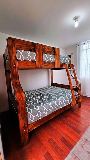 Uma cama beliche com escada, estrutura de madeira e roupa de cama estampada em um quarto com piso de madeira e uma janela.