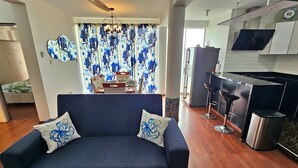 A modern living room with a sofa, a dining area with a table and chairs, and a kitchen with a bar area.