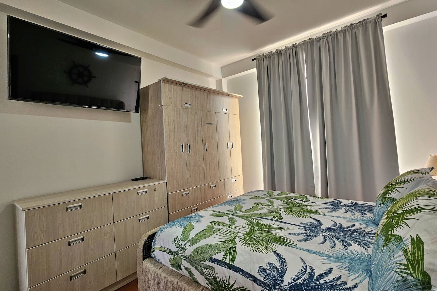 Ein Schlafzimmer mit einem Bett, einem Kleiderschrank, einem Fernseher und einem Fenster mit Vorhängen.