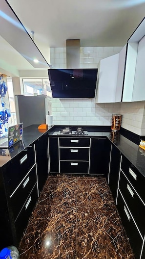 Cozinha com armários pretos, fogão a gás e paredes com azulejos brancos.