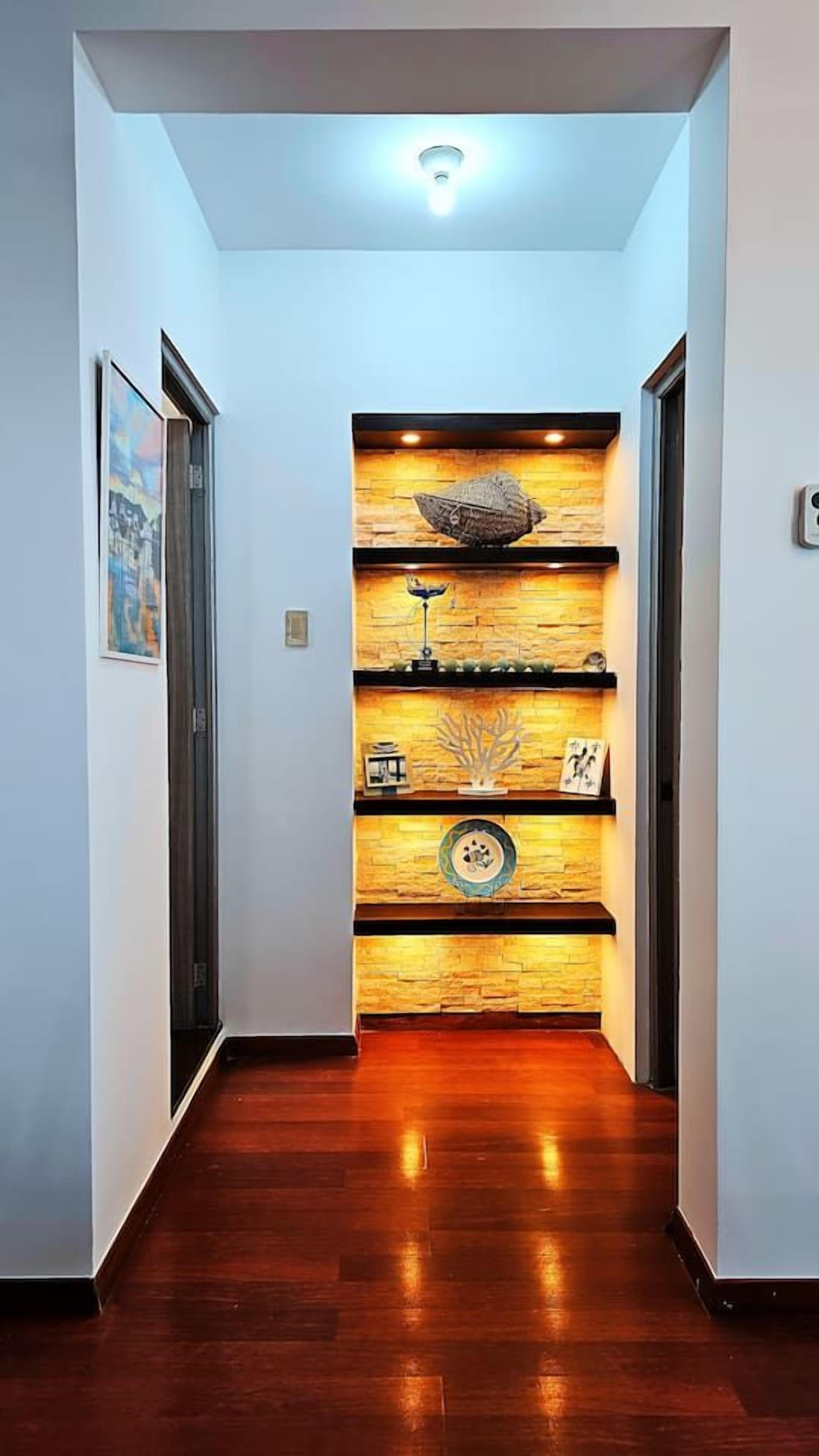 Een gang met houten vloer, een wandplank met decoratieve voorwerpen, en een plafondlamp.