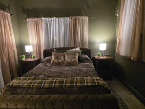 A bedroom with a large bed, two bedside tables, a lamp on each, and curtains on the windows.