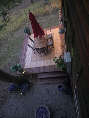 A wooden deck with a table and chairs, surrounded by potted plants and a red umbrella. - Cozy cottage close to two lakes, Bigfork and Glacier park. Pet friendly. (Kalispell)