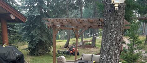 A covered outdoor seating area with a pergola, a grill, and a table with chairs.