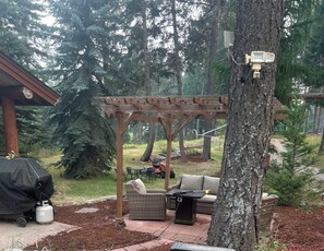 A covered outdoor seating area with a pergola, a grill, and a table with chairs.
