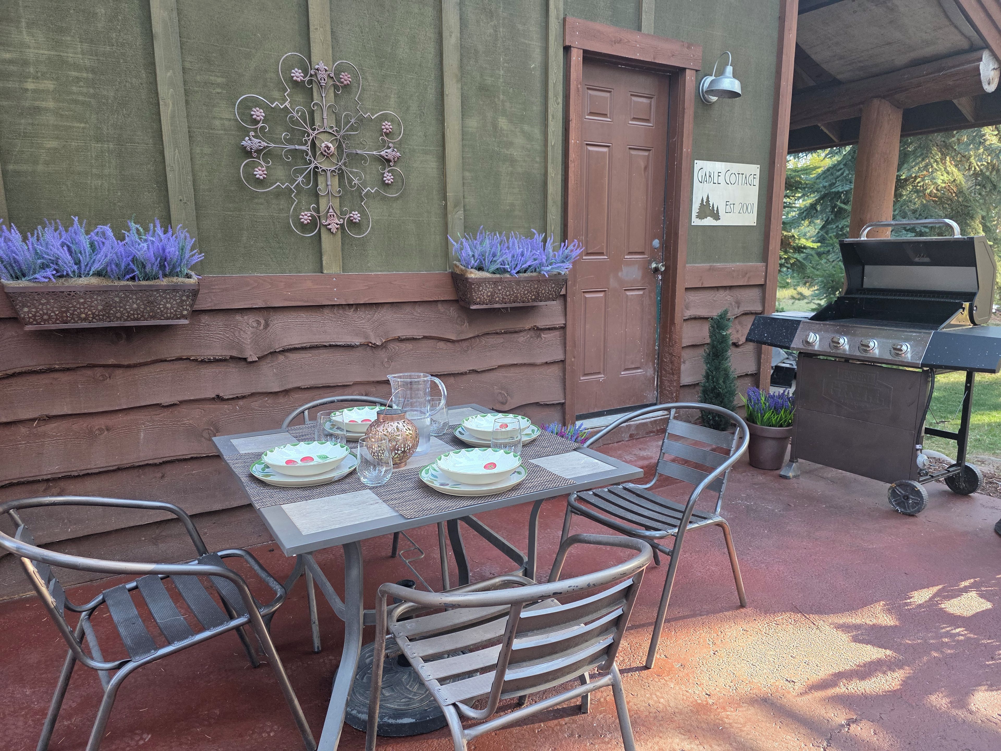 An outdoor patio with a table set for four, metal chairs, a grill, and decorative planters.