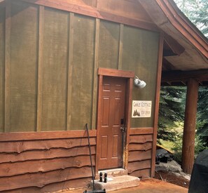 A rustic cabin with a wooden door, a sign indicating 'Gable Cottage,' and a metal lantern on the porch.