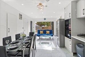 A modern kitchen with a dining area, featuring a blue sofa, a glass-top coffee table, and a dining table set for six.