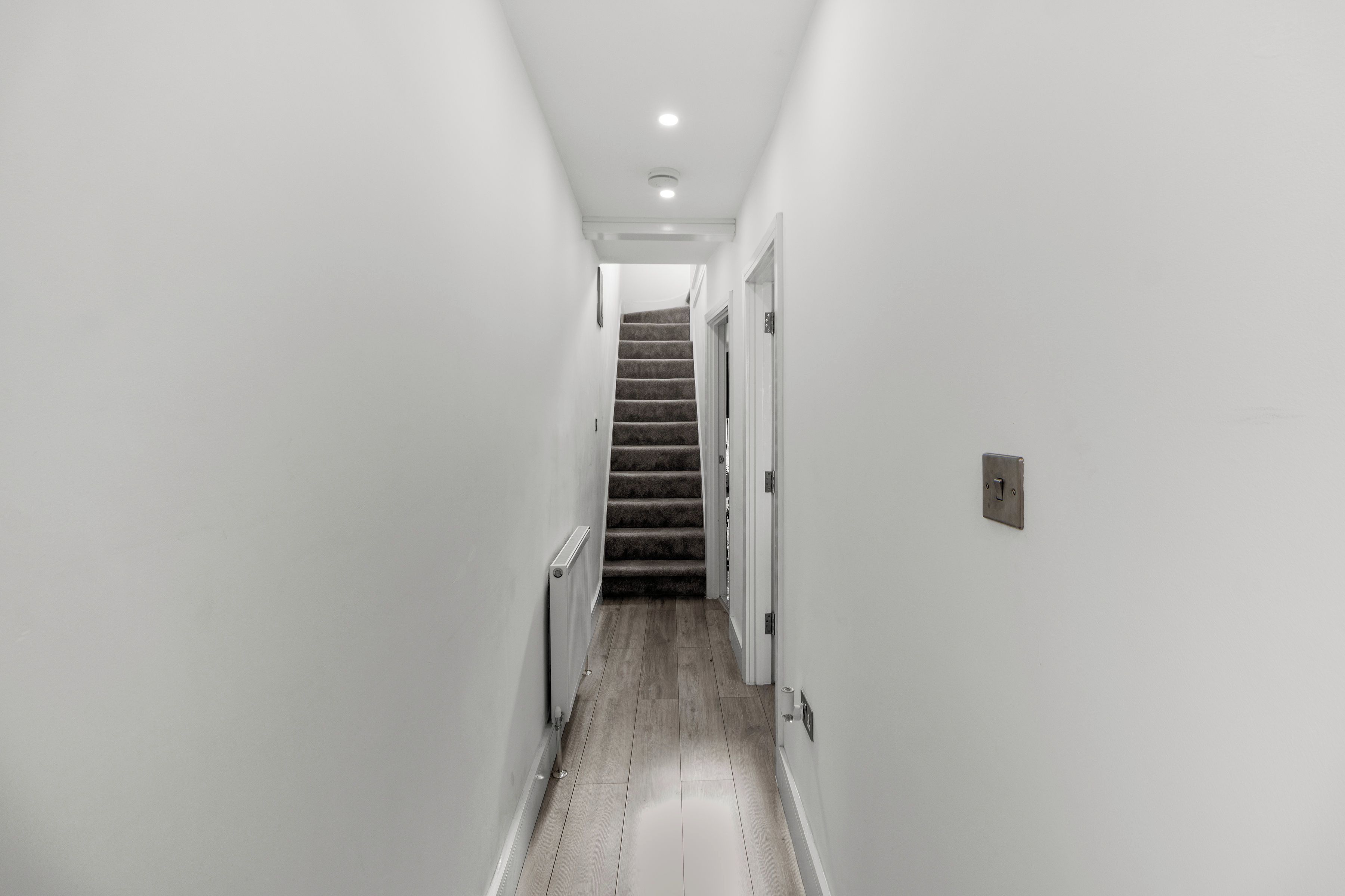 A narrow hallway with a carpeted staircase leading to a door.
