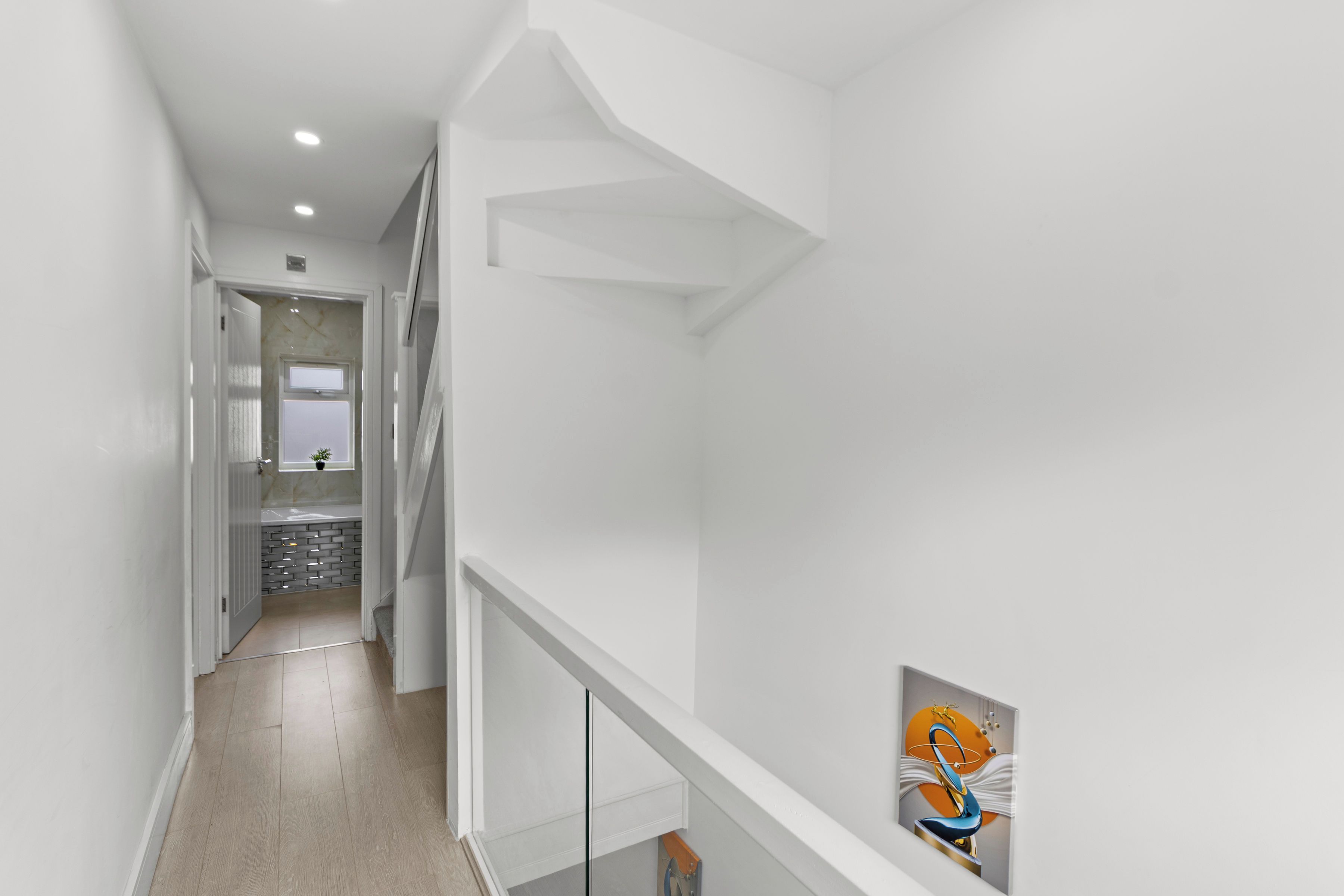 A modern interior with a staircase, a hallway leading to a bathroom, and a wall-mounted artwork.