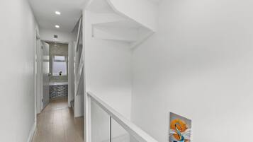 A modern interior with a staircase, a hallway leading to a bathroom, and a wall-mounted artwork.