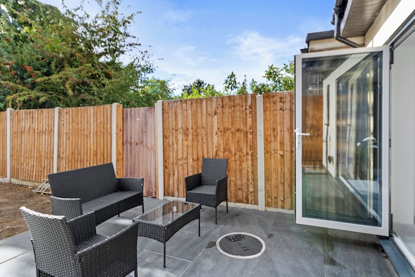 A patio with wicker furniture, a glass table, and a wooden fence.