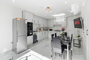 Una cocina moderna con armarios blancos, horno empotrado y comedor con mesa para dos.